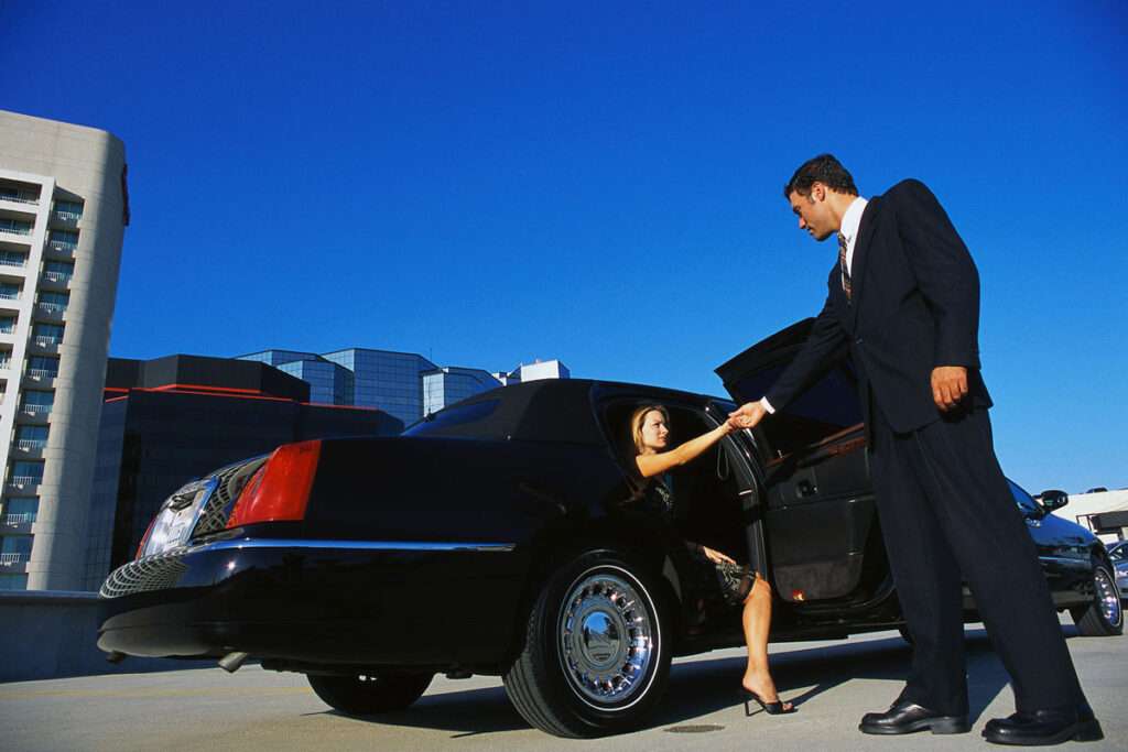 A chauffeur helps a woman out of her private car