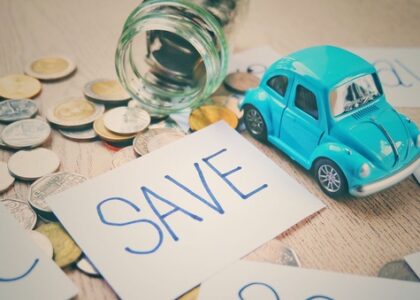 A jar with coins spilled on a table. A card that says save and a blue toy car