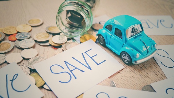 A jar with coins spilled on a table. A card that says save and a blue toy car